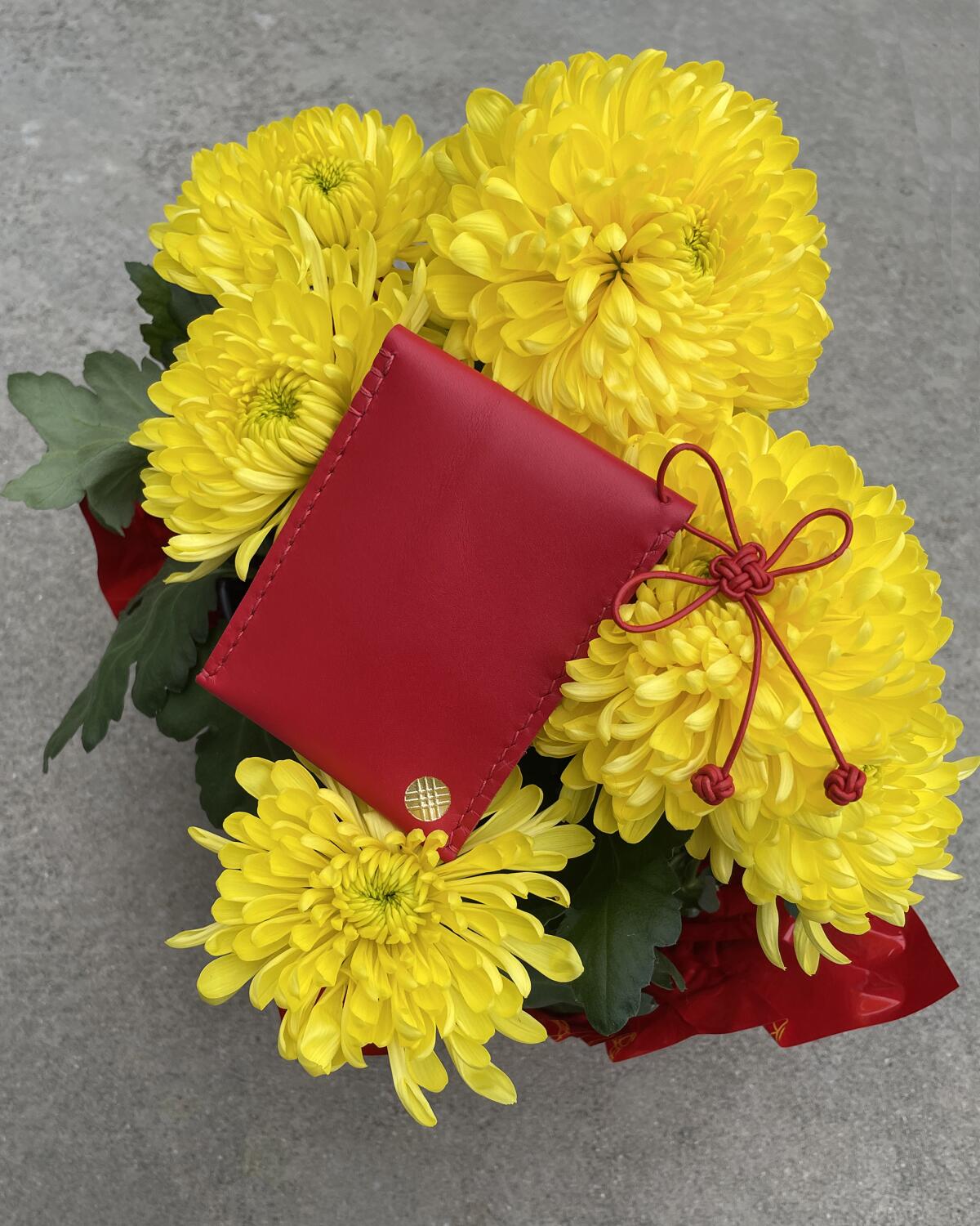 A red leather bag sitting on yellow chrysanthemums
