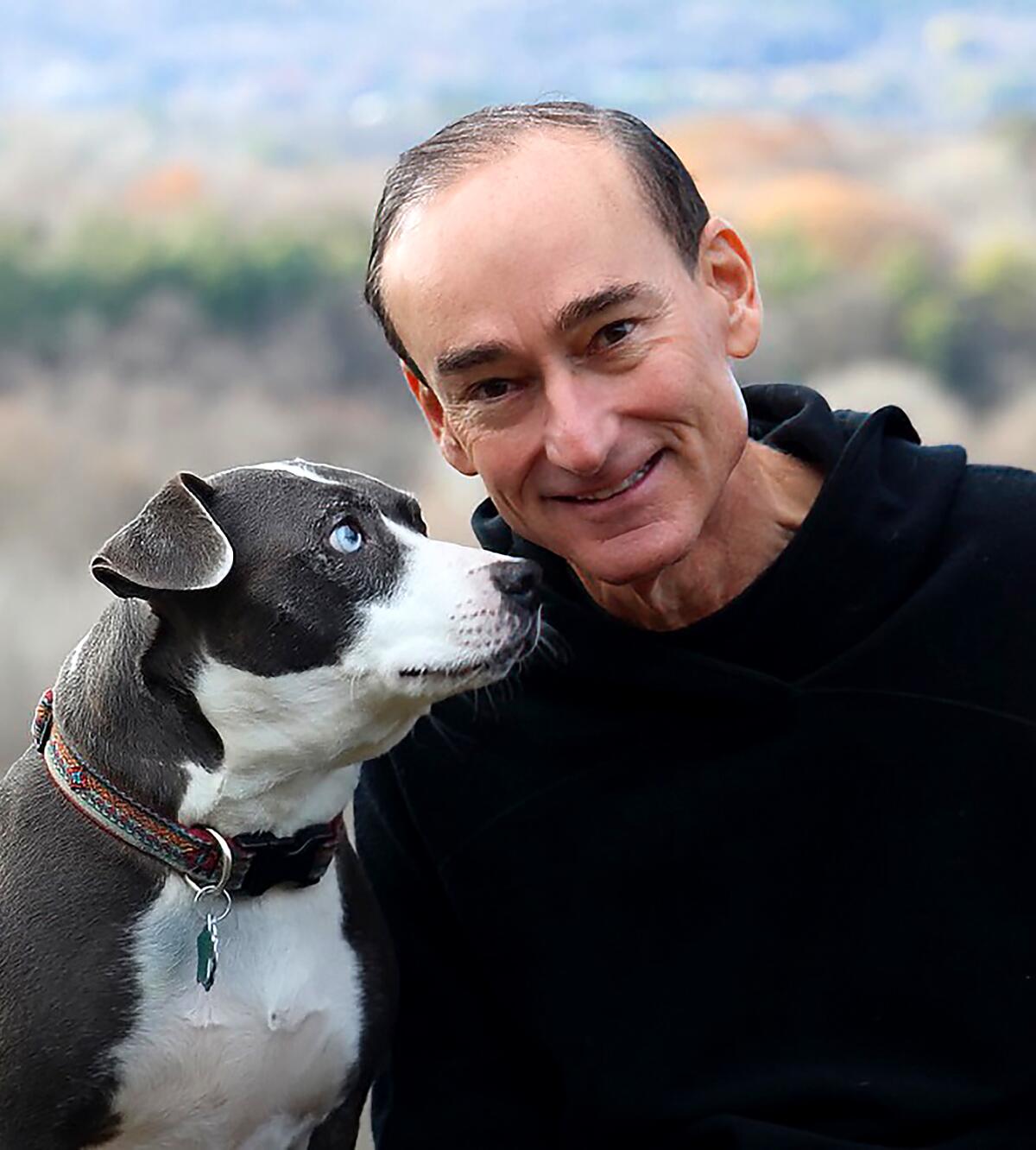 Chris Bohjalian, in a black hoodie, poses for a photo with his dog.
