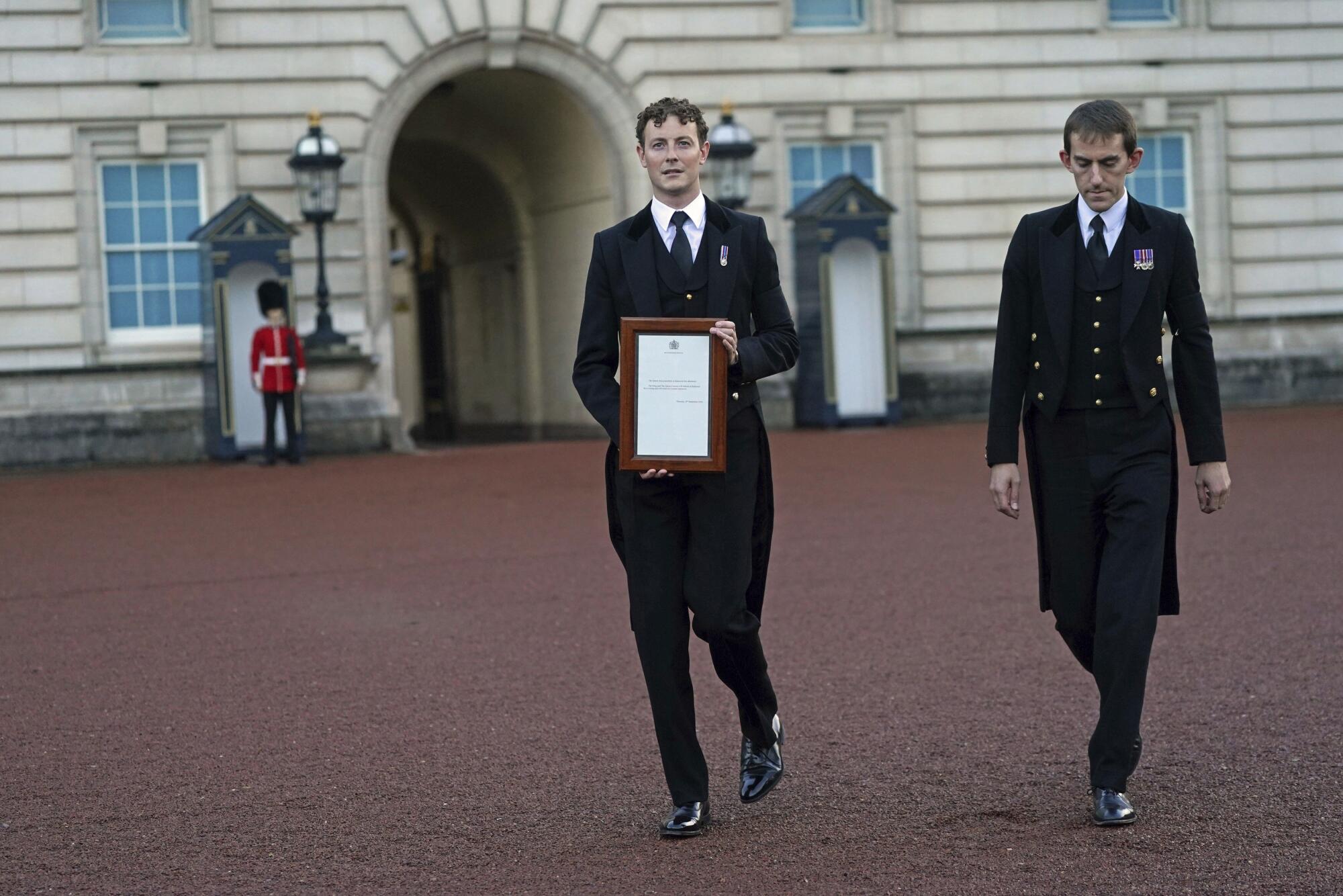 A member of royal household staff posts a notice on the gates of the Buckingham Palace in London.