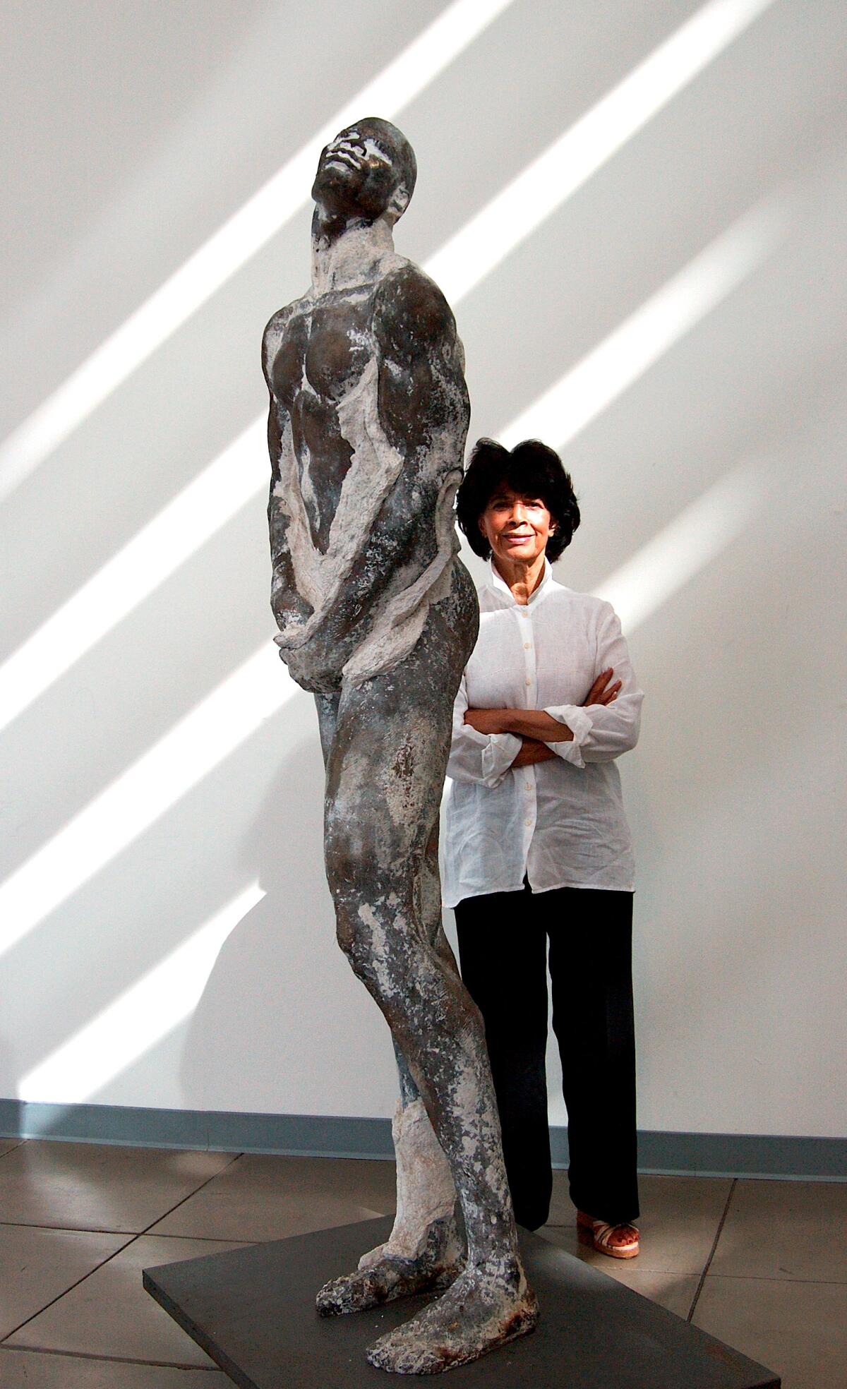 A woman in a white shirt next to a tall sculpture of a man