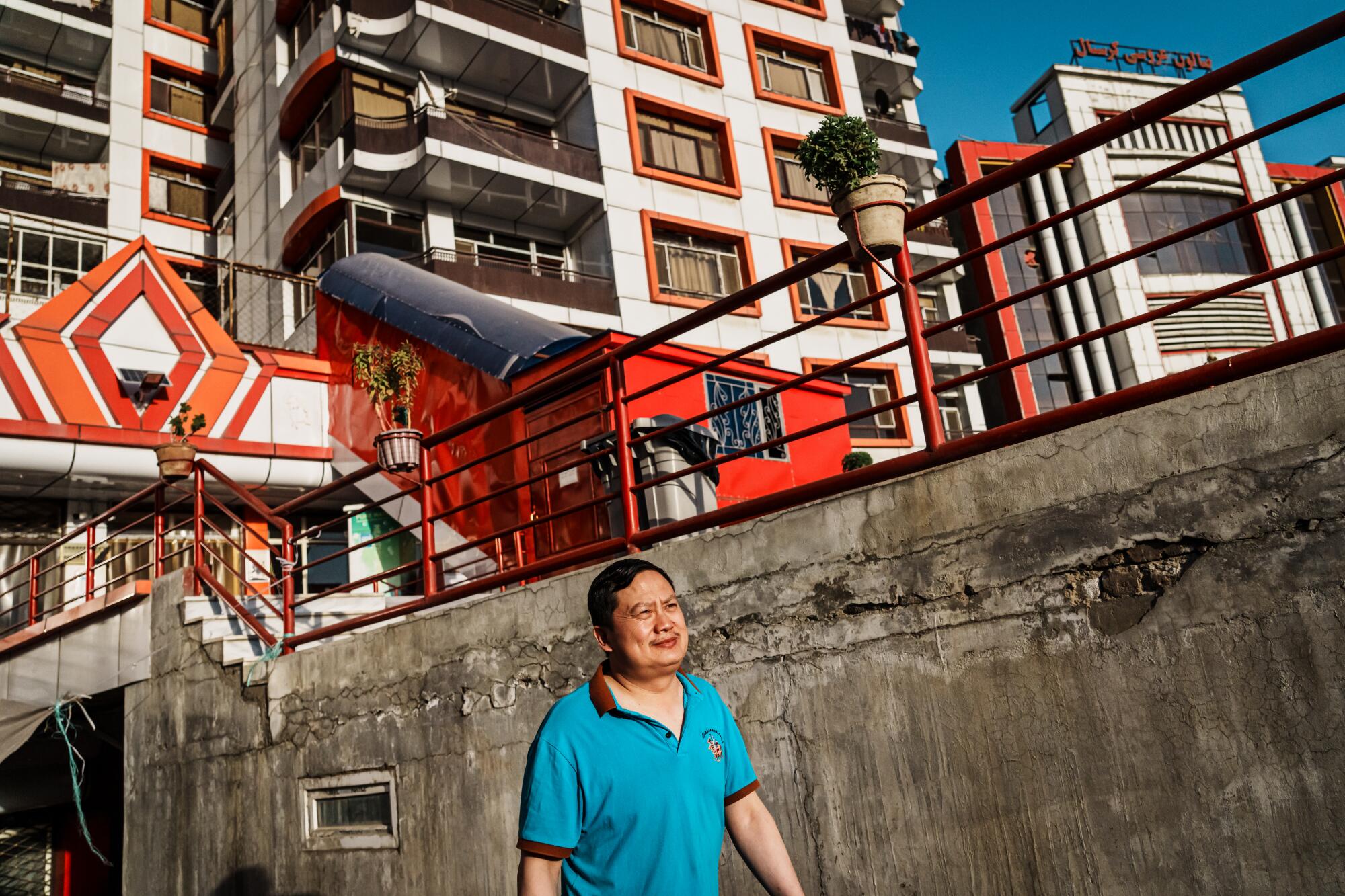 A man in a blue polo shirt stands in front of a group of high-rise buildings 