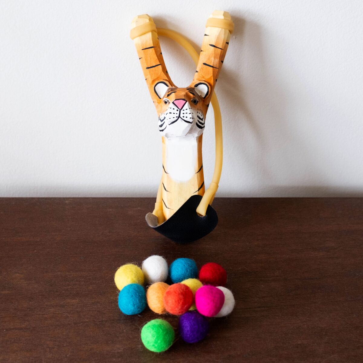 A slingshot shaped like a tiger with outstretched paws and 12 felt balls