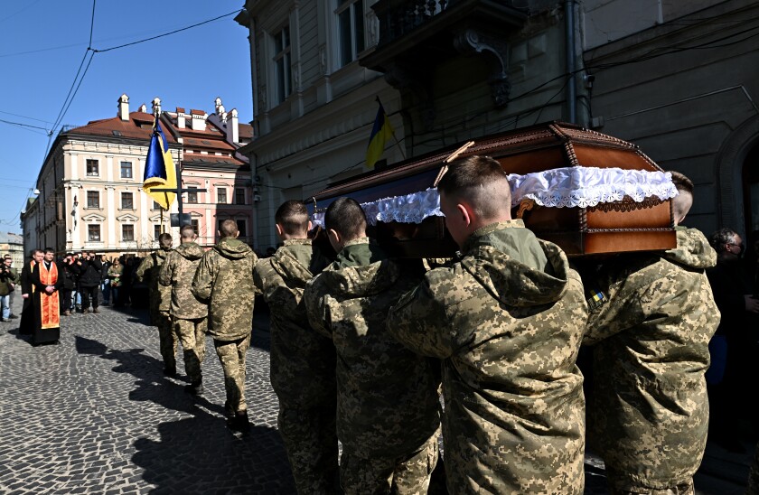 Ukrainian soldiers carry a casket in a street.