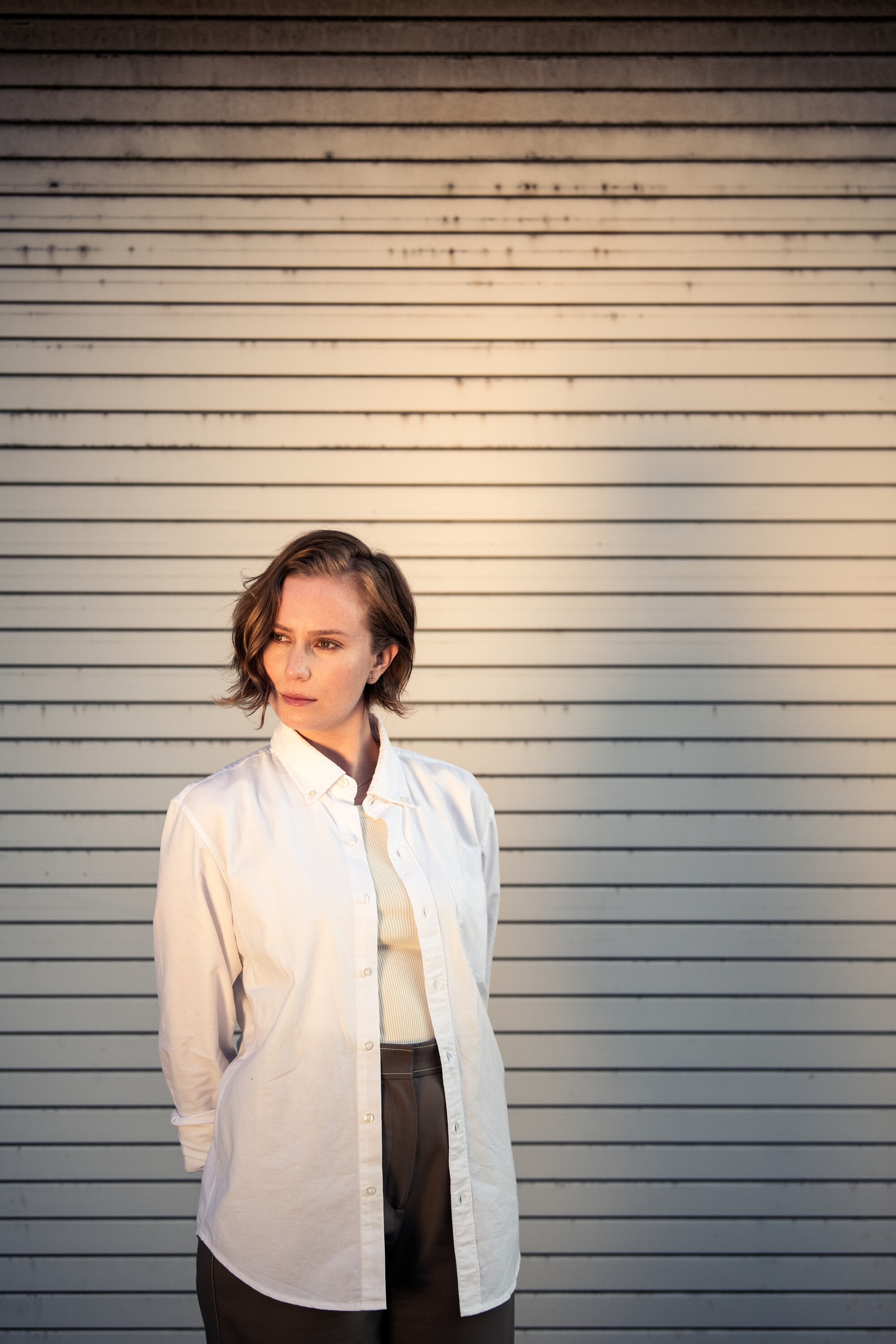 A woman poses for her portrait in front of a slatted wall.