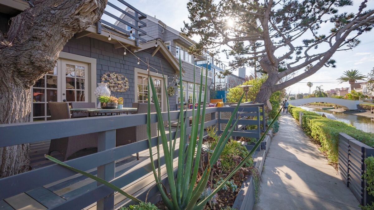A blue-shingled home with a patio and matching blue fence faces the canal in Venice, California