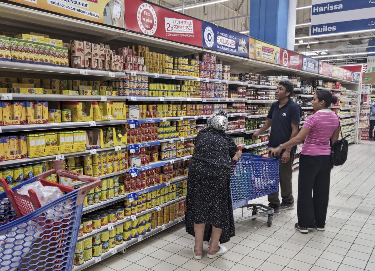 People shop at a supermarket, in Tunis, Tunisia, Monday, Oct. 10, 2022. Sugar, vegetable oil, rice, even bottled water – Tunisians have suffered shortages of multiple staples in recent weeks. And costs are soaring on products still available. (AP Photo/Hassene Dridi)