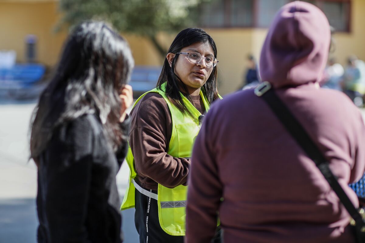 A woman wearing a yellow vest and glasses speaks to two people at the fairgrounds in Watsonville.