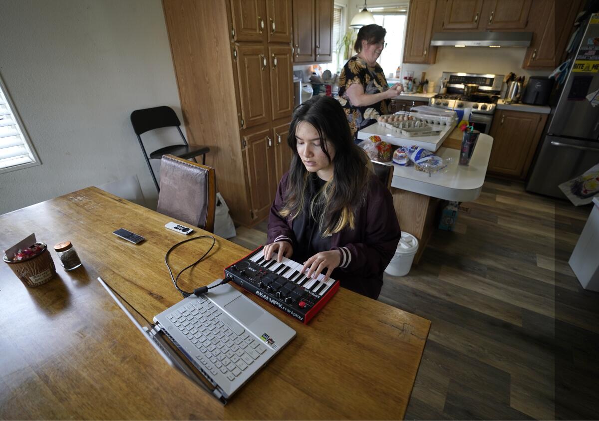 Summer Oriyavong uses a keyboard while her mother, Sheri Oriyavong, cooks in the kitchen at their Rio Linda, Calif., home.
