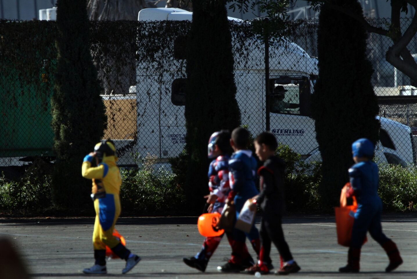 Trucks using Terminal Island Freeway pass close to the playground at Hudson Elementary as pupils line up for their Halloween parade.