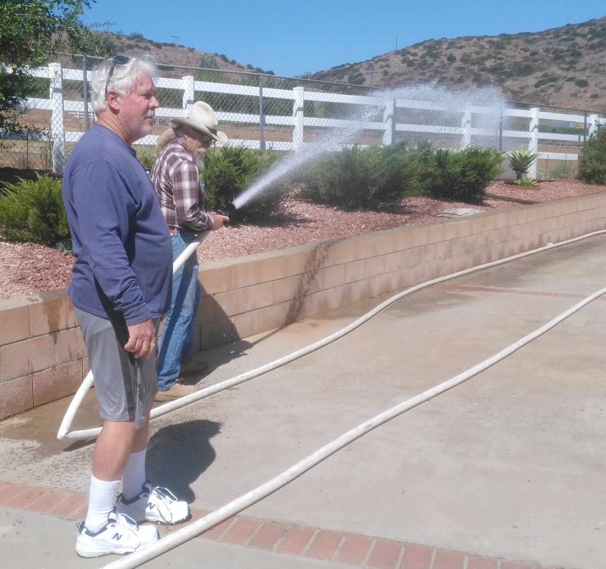 Ramona homeowner Dan Summers, left, talks about safety features at his home while Jim Cooper uses a hose attached to a 5,000-gallon water tank on Summers’ property. Firefighters are able to connect to the hose in a fire emergency.