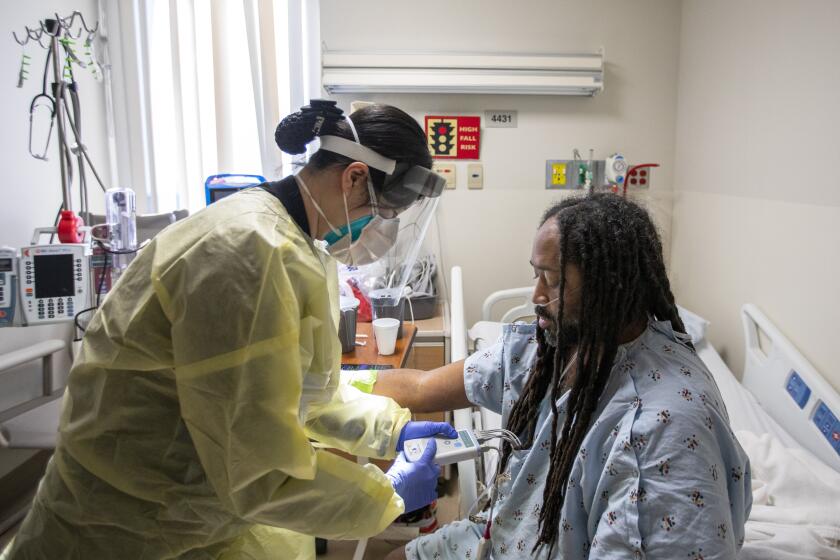 TORRANCE, CA - JANUARY 11: Registered nurse Giyun Kim, left, works with covid19 patient Marcus Miller, 44, right, of Carson in the covid unit at Providence Little Company of Mary Medical Center on Tuesday, Jan. 11, 2022 in Torrance, CA. (Francine Orr / Los Angeles Times)