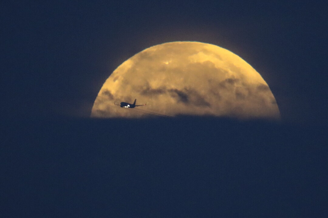 Un aeroplano attraversa davanti alla luna piena mentre tramonta