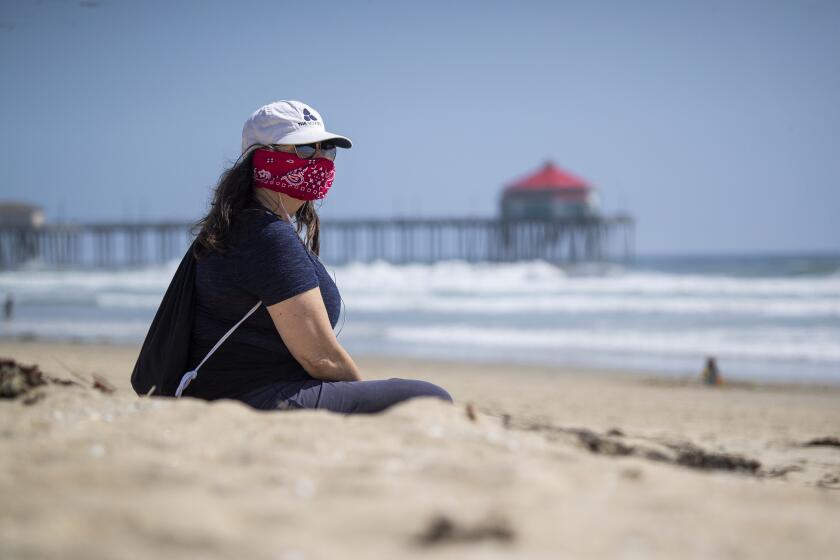 HUNTINGTON BEACH, CALIF. -- THURSDAY, APRIL 2, 2020: Kelly Beita, of Huntington Beach, wears a bandana to help protect her and others from possible Coronavirus exposure as she takes a break from working from home, to relax and walk on the beach in Huntington Beach Thursday, April 2, 2020. Beita said she read that it's possible Coronavirus is in the water and the air at the beach and that her friend is making one for her. (Allen J. Schaben / Los Angeles Times)