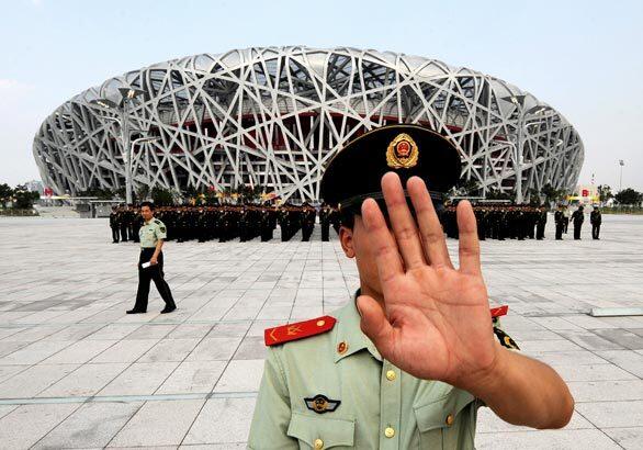 A Chinese paramilitary policeman attempts to block photos from being taken of a military parade rehearsal outside Beijing's "Bird's Nest" National Stadium, the site of the upcoming Olympics. China has vowed to step up security for the Games and said that with up to 80 world leaders expected to attend the Aug. 8 opening ceremony, it faces a huge responsibility to defend its own people, Olympic athletes and visiting dignitaries.