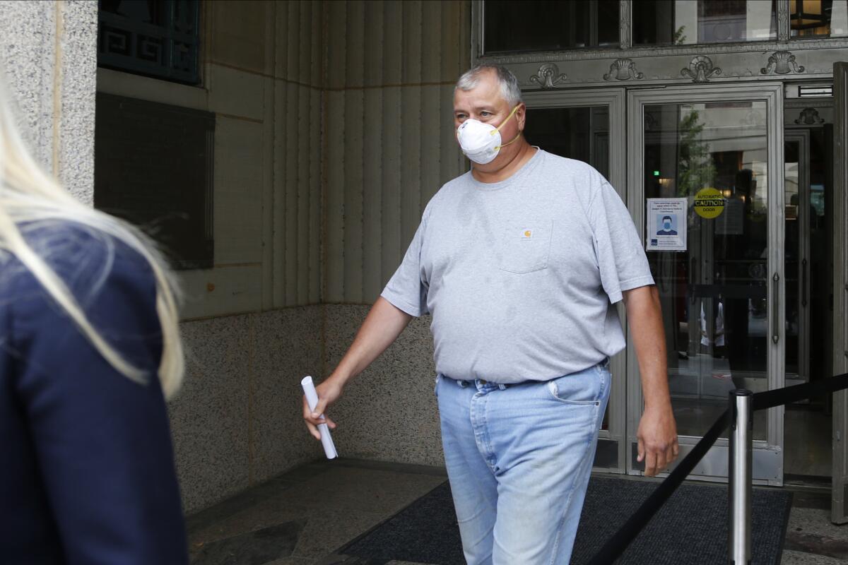 A man in jeans, T-shirt and facemask walks out of a building