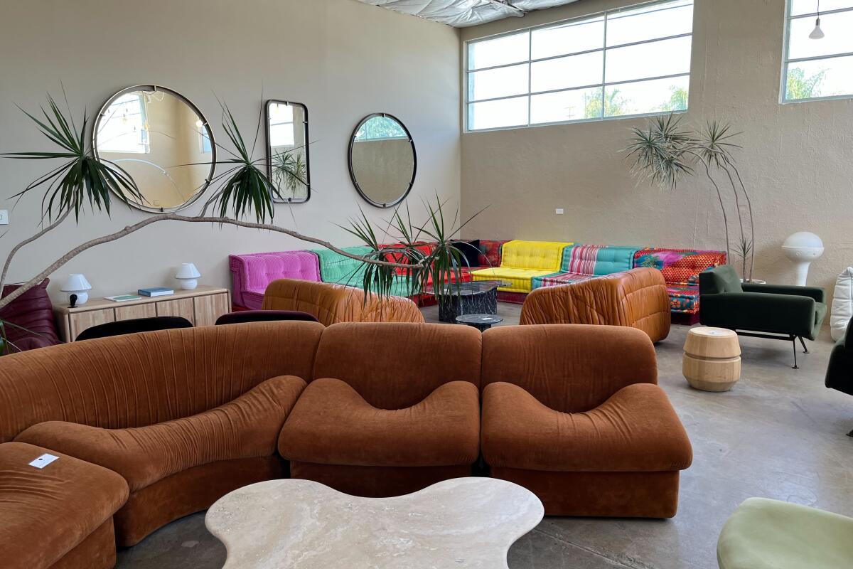 A rust-colored sectional sofa and, behind it, a multicolored sectional sofa under mirrors on the wall