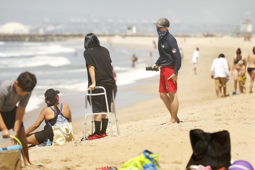 SEAL BEACH-CA-MAY 21, 2020: A Seal Beach Lifeguard politely reminds beach goers to keep in motion while enjoying a day at Seal Beach on Thursday, May 21, 2020, as the city of Seal Beach extends the hours they are open. (Christina House / Los Angeles Times)