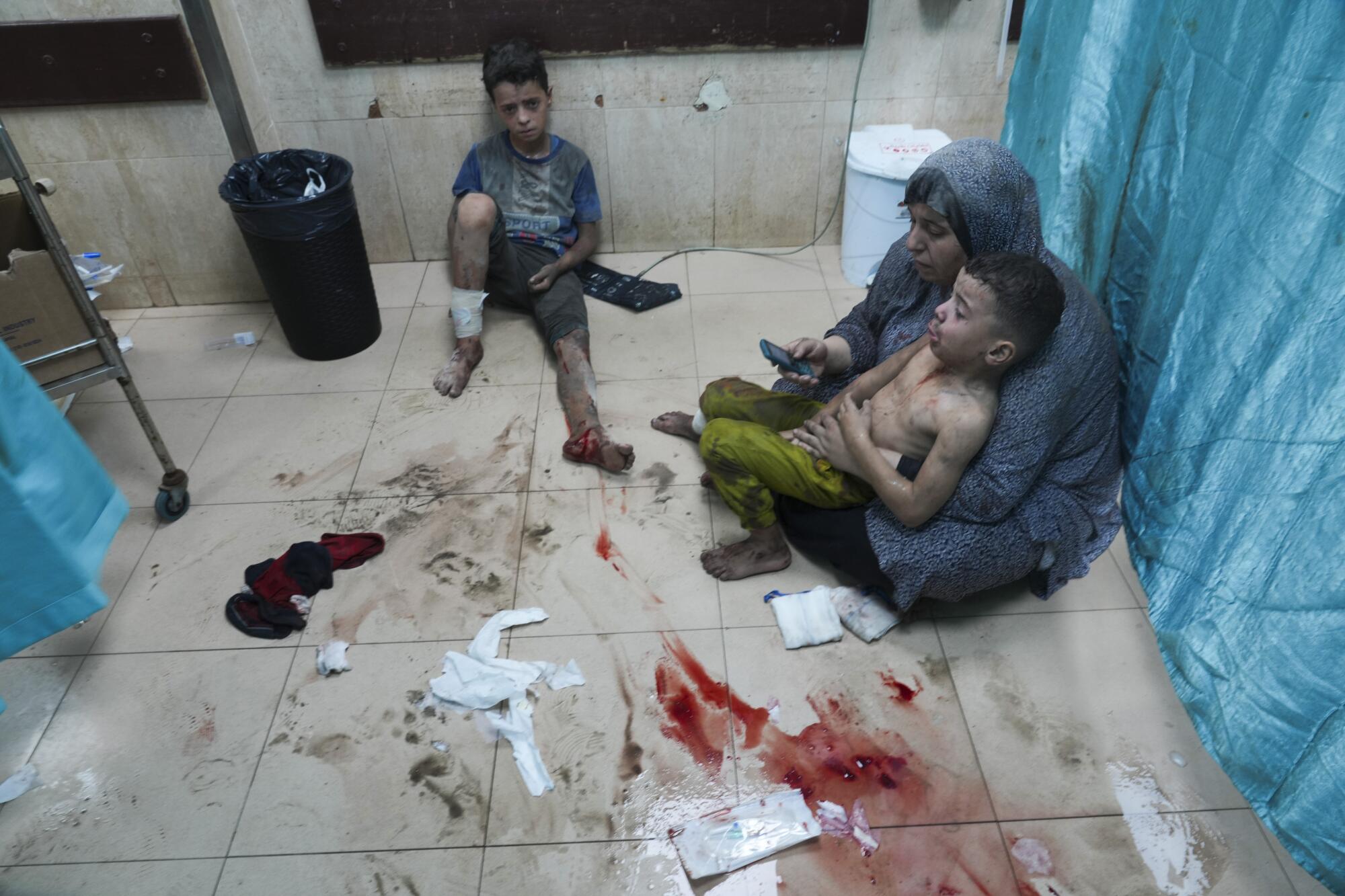 An adult and two children sit on the bloodstained floor of a Gaza hospital.