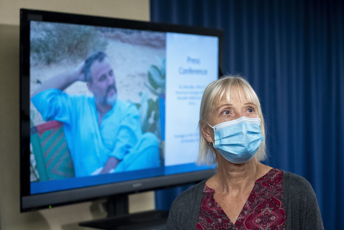 FILE - Els Woodke speaks about the 2016 kidnapping of her husband Jeffrey Woodke, photo on video monitor, in West Africa, during a news conference in Washington, Nov. 17, 2021. The Biden administration says the American aid worker who was kidnapped in Niger six years ago has been released from custody. Jeffrey Woodke was kidnapped from his home in Abalak, Niger, in October 2016 by men who ambushed and killed his guards and forced him at gunpoint into their truck, where he was driven north toward Malis border. (AP Photo/Cliff Owen, File)