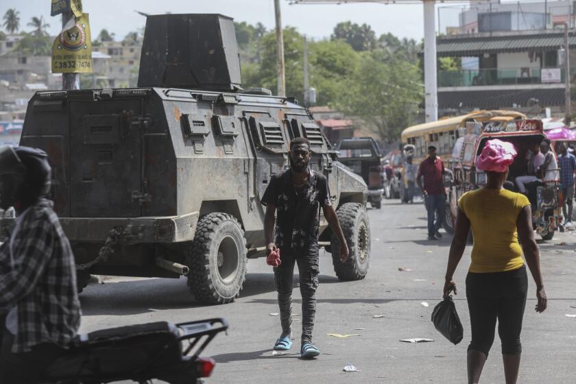 People walk past an armored police vehicle patrolling the streets in Port-au-Prince, Haiti, Monday, July 15, 2024. (AP Photo/Odelyn Joseph)