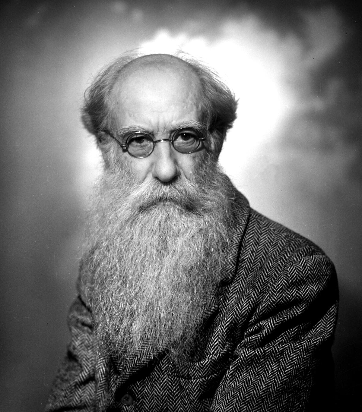 A photo portrait of a balding man with a long white beard and wearing glasses.