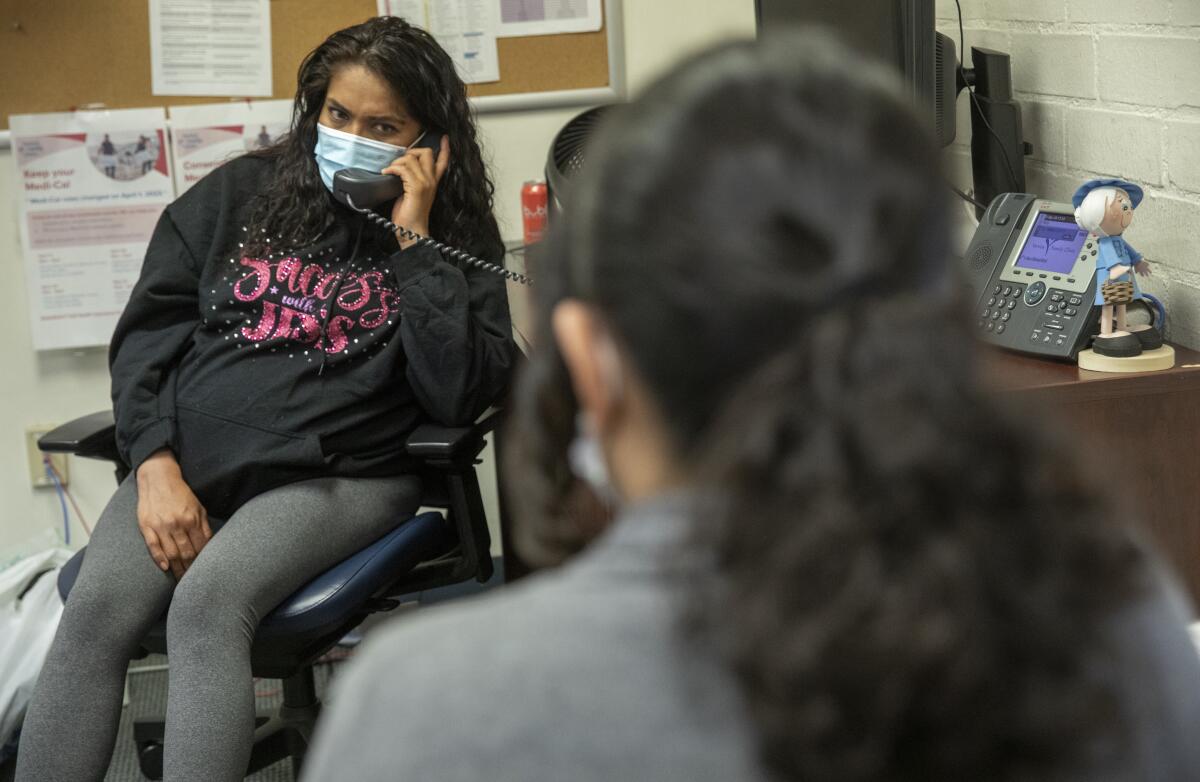 A woman wearing a medical mask holds a phone receiver in an office. 