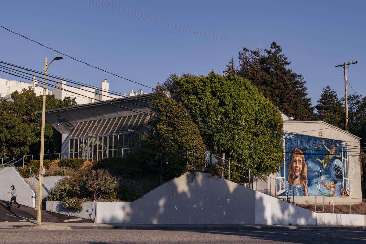 A building surrounded by trees with a mural of a young girl on one wall