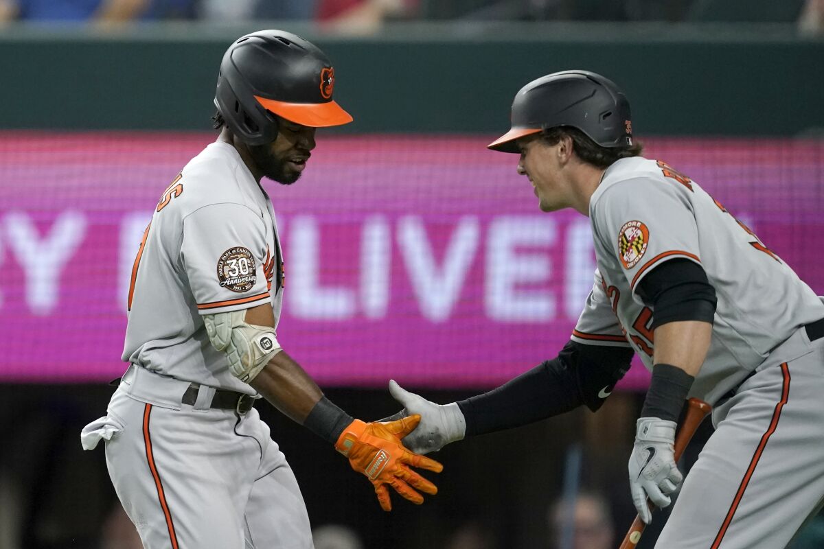 Baltimore Orioles' Cedric Mullins, left, and Adley Rutschman, right, celebrate after Mullins hit a lead-off home run in the first inning of a baseball game against the Texas Rangers, Monday, Aug. 1, 2022, in Arlington, Texas. (AP Photo/Tony Gutierrez)
