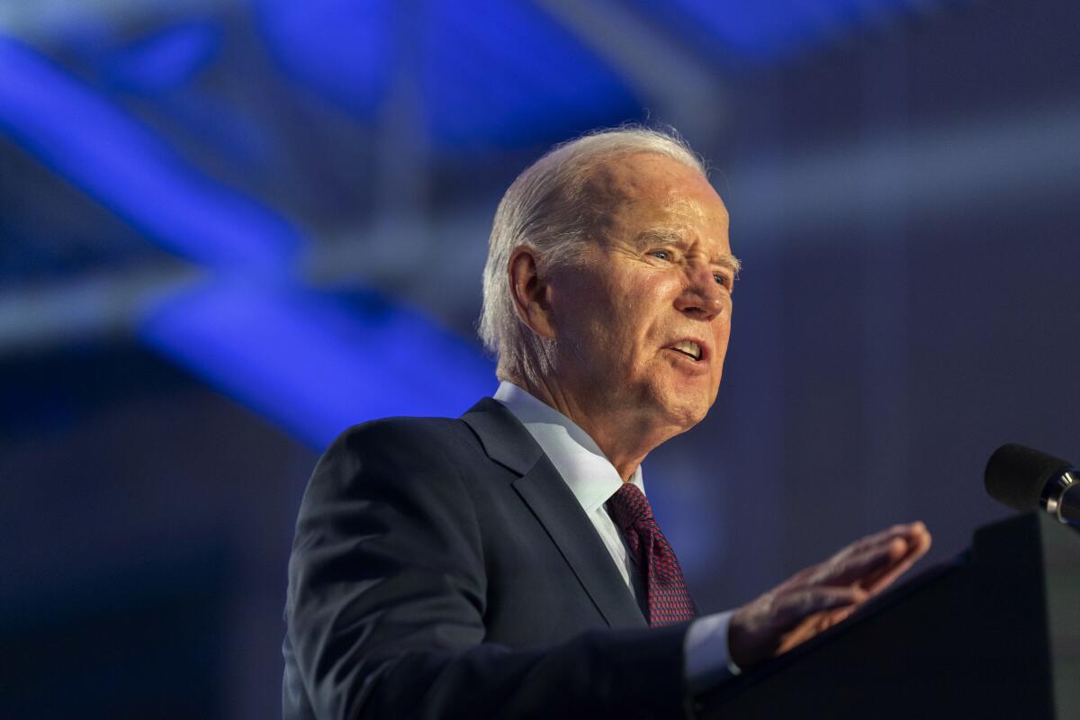 President Biden speaking at a podium, against a blurred blue and gray background 