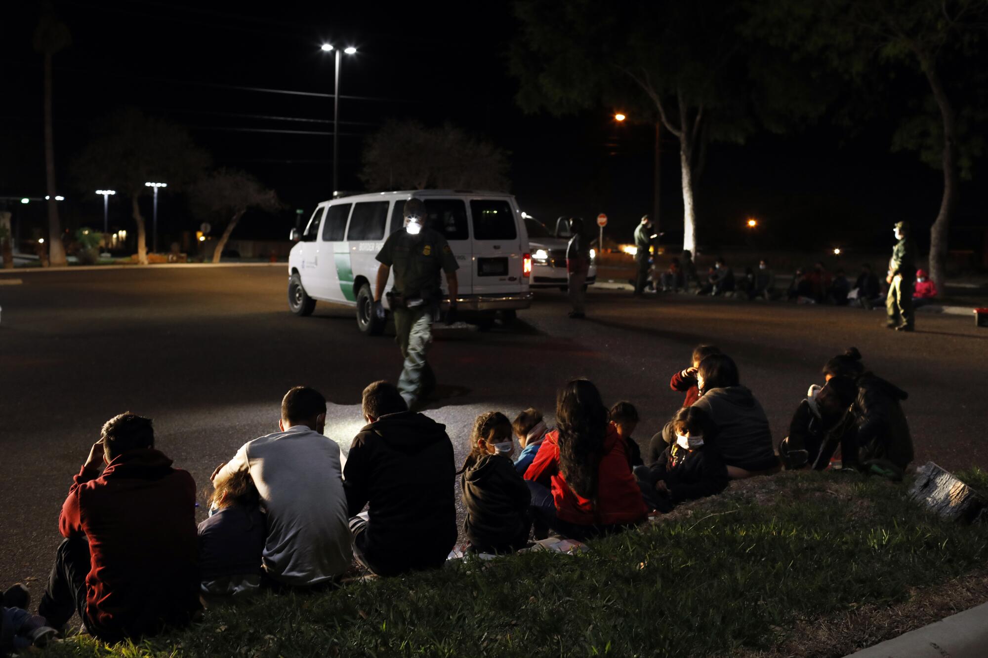 Families sit on a curb, waiting to be processed by Border Patrol 