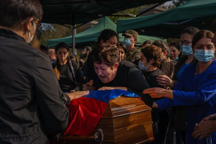 YEREVAN, ARMENIA -- OCTOBER 15, 2020: A woman wails over a casket as family and friends surround her to comfort her as they gather to mourn the loss of Kristapor Artin and Suren Vanyan, both volunteer fighters who lost their lives to the Nagorno-Karabakh war, at the Yerablur Military Memorial Cemetery in Yerevan, Armenia, on Thursday Oct. 15, 2020. The conflict, which began on Sept, 27, is between Azerbaijani and Armenian forces over Nagorno-Karabakh D a disputed region, which is also internationally recognized as part of Azerbaijan D has killed hundreds including dozens of civilians from both sides, and the death toll continues to mount. (Marcus Yam / Los Angeles Times)