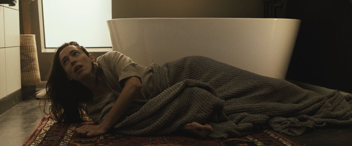 A woman lies on the floor in front of a bathtub.