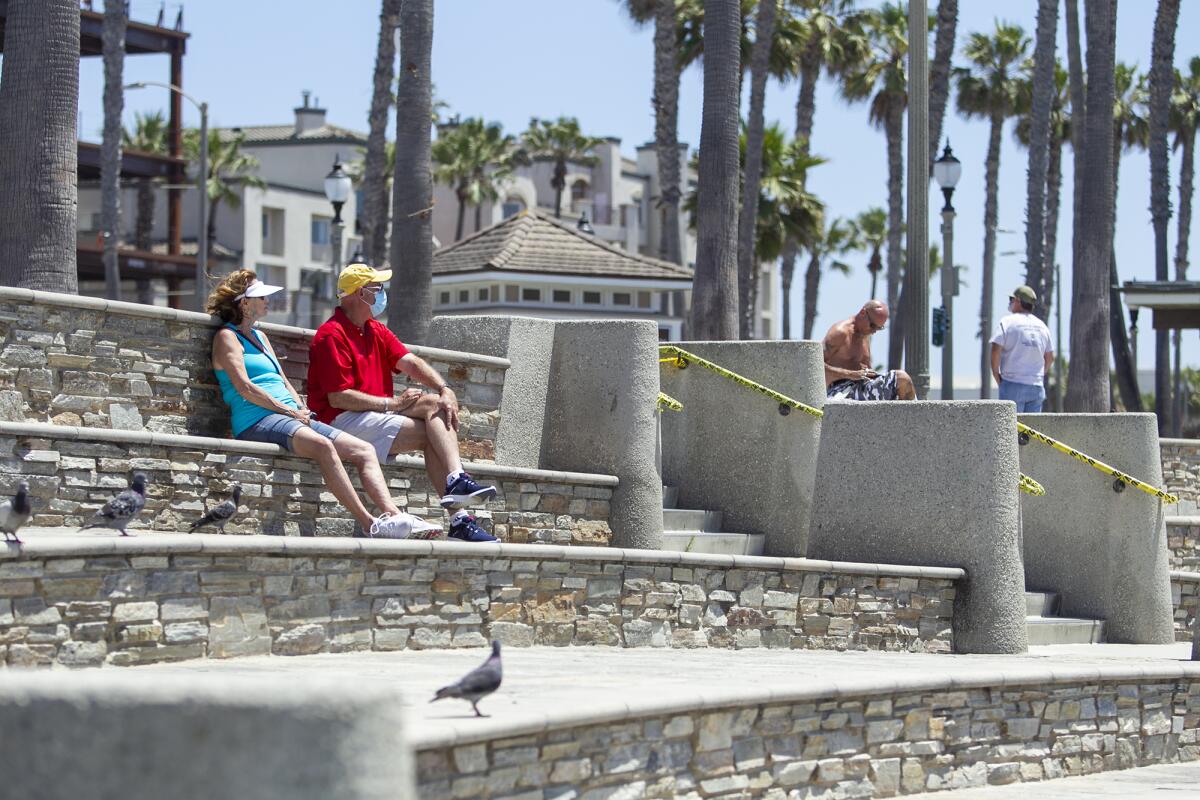 Darlene Dunn, left, and Tom Pence sit on a bench at the Huntington Beach Pier Plaza on Tuesday.
