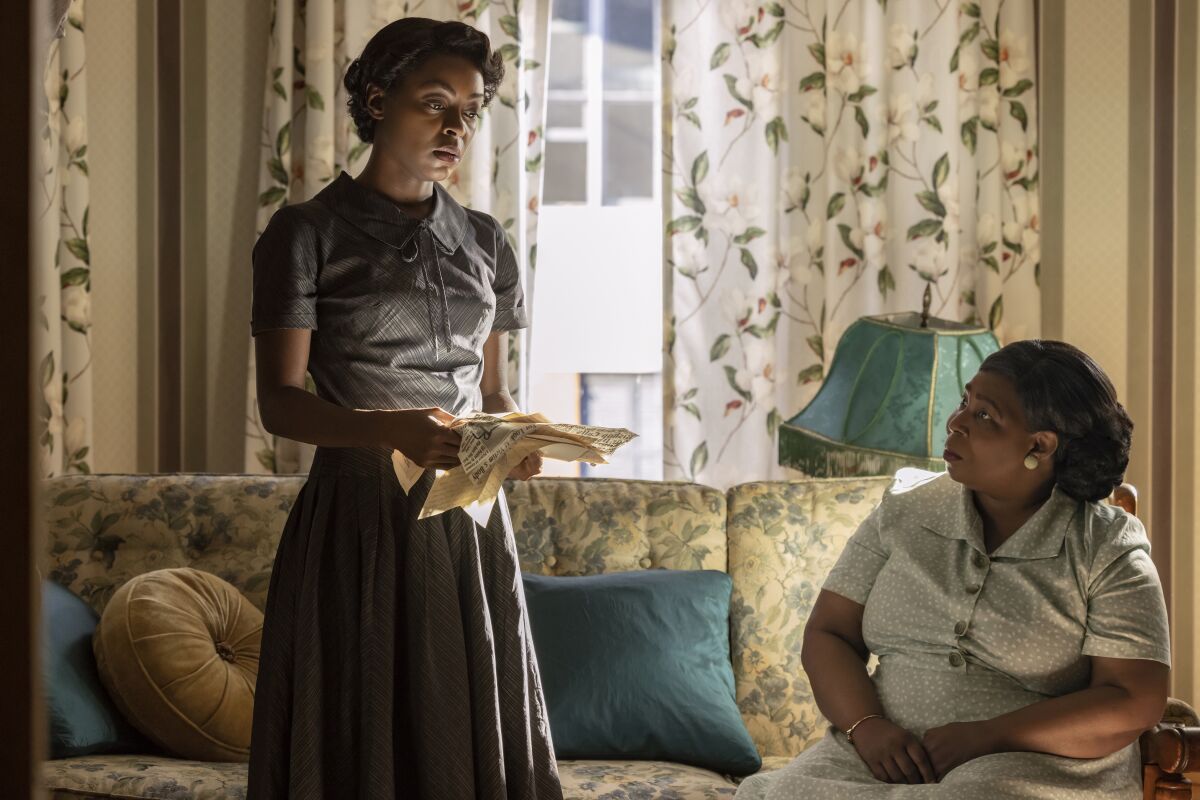 A seated and a standing woman holding papers in a 1950s living room