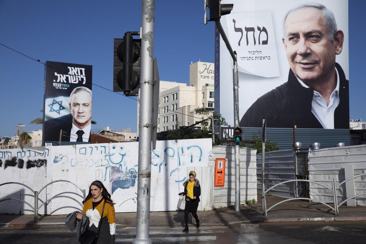 People walk next to election campaign billboards last month showing Israeli Prime Minister Benjamin Netanyahu, right, and Benny Gantz, left, in Bnei Brak, Israel. 