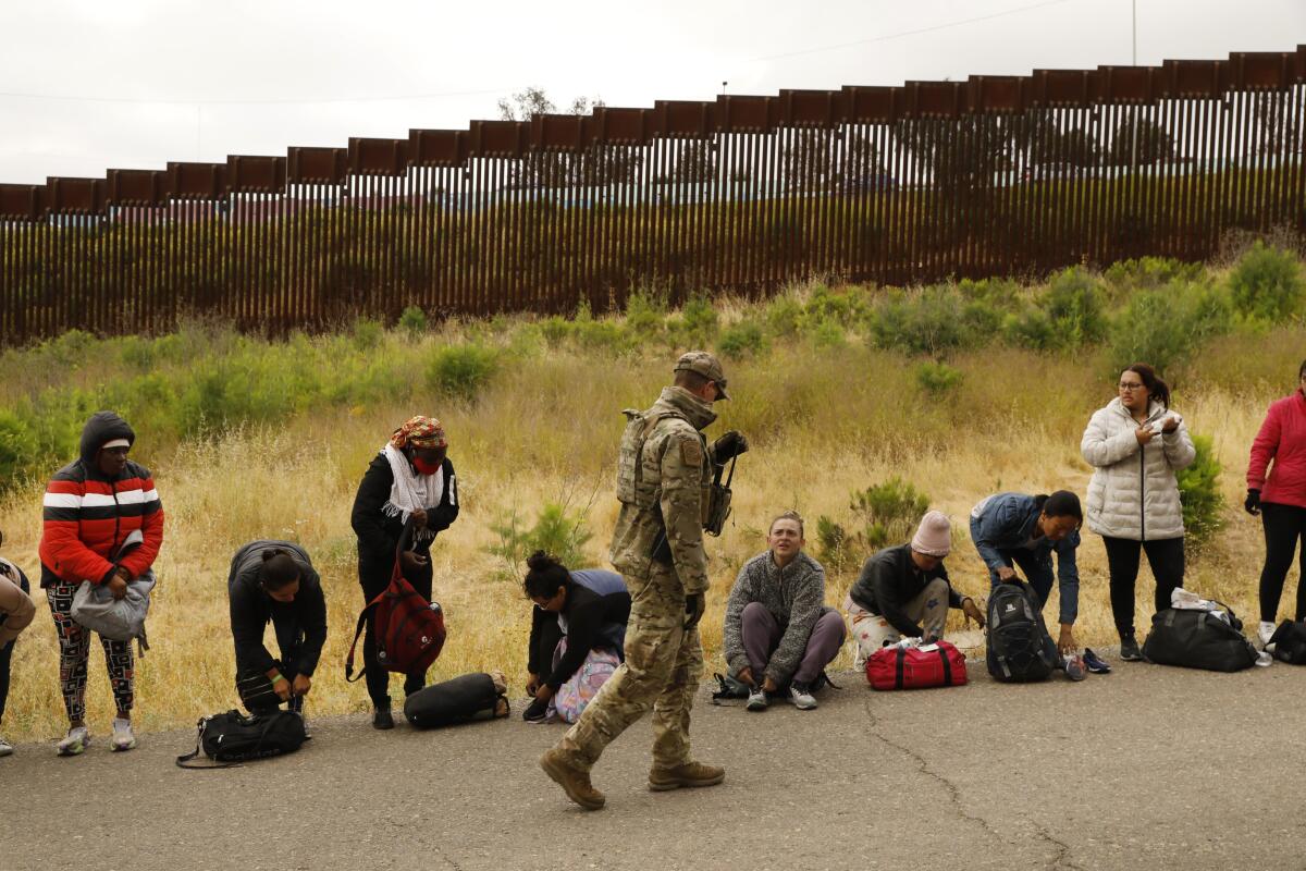 Border Patrol agent walks past a line of people with small backpacks.