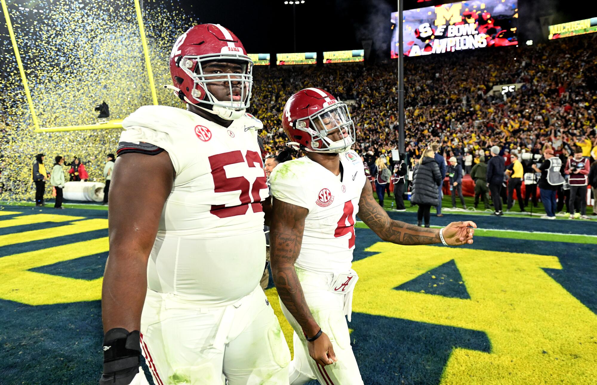Alabama offensive lineman Tyler Booker and quarterback Jalen Milroe walk off the field after losing to Michigan.
