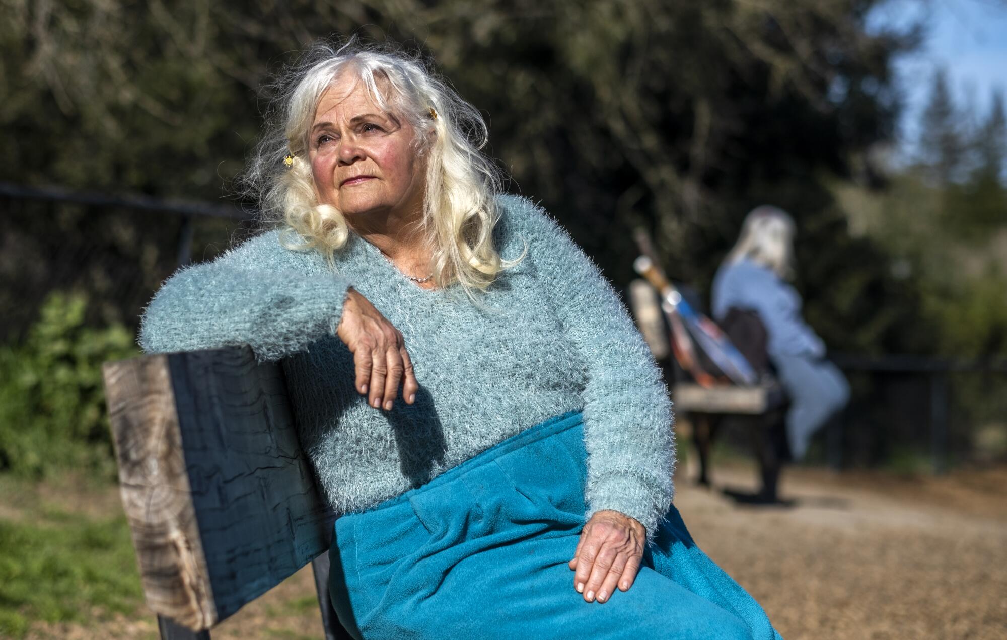 A woman sitting on a park bench looks over her shoulder into the distance.