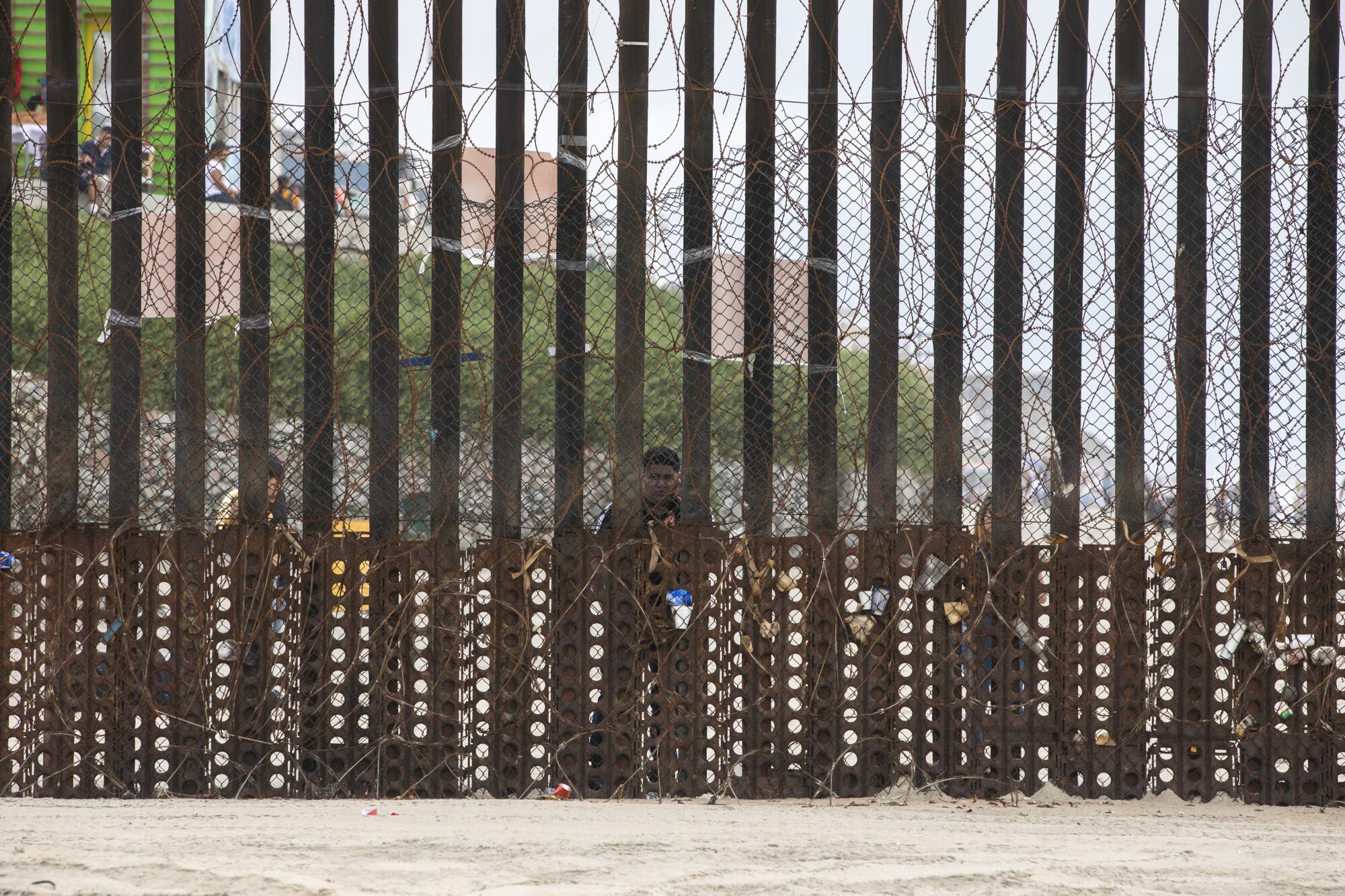 A man stands at the border fence, looking through.