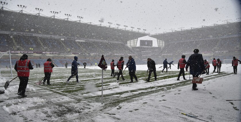 Empleados despejan la nieve en el campo del estadio Turf Moor previo al partido entre Burnley y Tottenham por la Liga Premier, el domingo 28 de noviembre de 2021. (AP Foto/Rui Vieira)