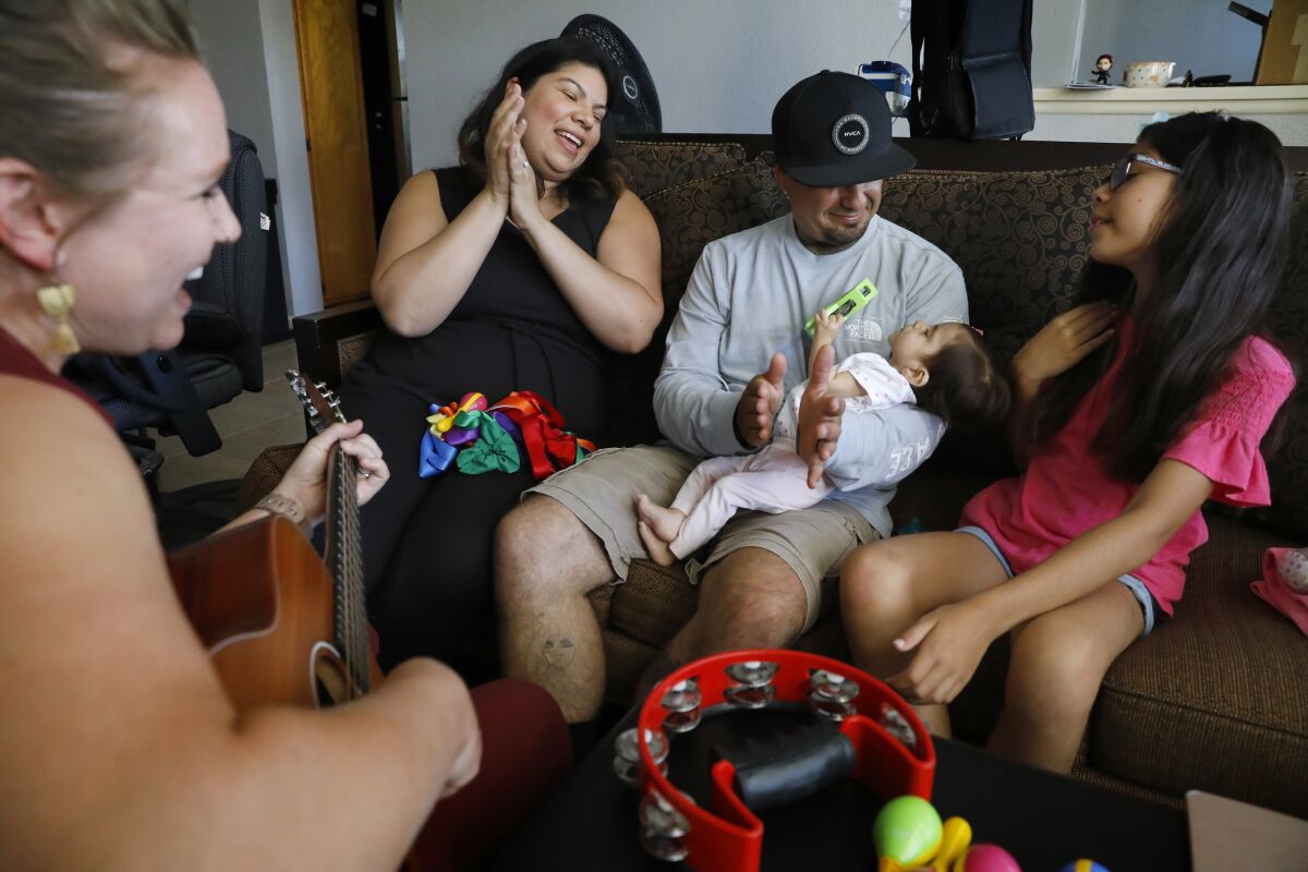 Music therapist Lindsay Zehren, left, performs a song with Bianca Zaragoza, second from left, and Danny Zaragoza, who is holding their daughter Ari, while Bianca's daughter Ava Morales, 9, sings along