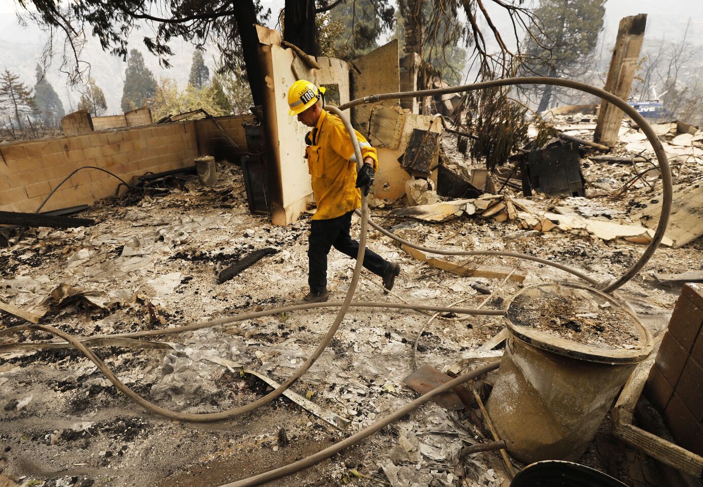 Los Angeles County Firefighter Brandon Smith runs hose through a burned out home to complete mop-up in the Lake Fire.