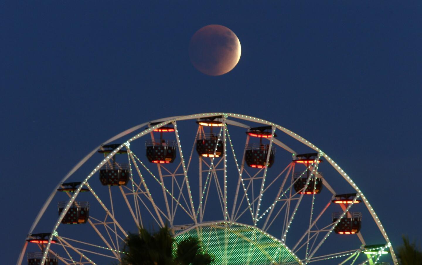 The "super moon" is nearly in total eclipse at 6:07pm September 27, 2015 as it rises behind the Ferris Wheel at the Irvine Spectrum mall in Irvine, CA.
