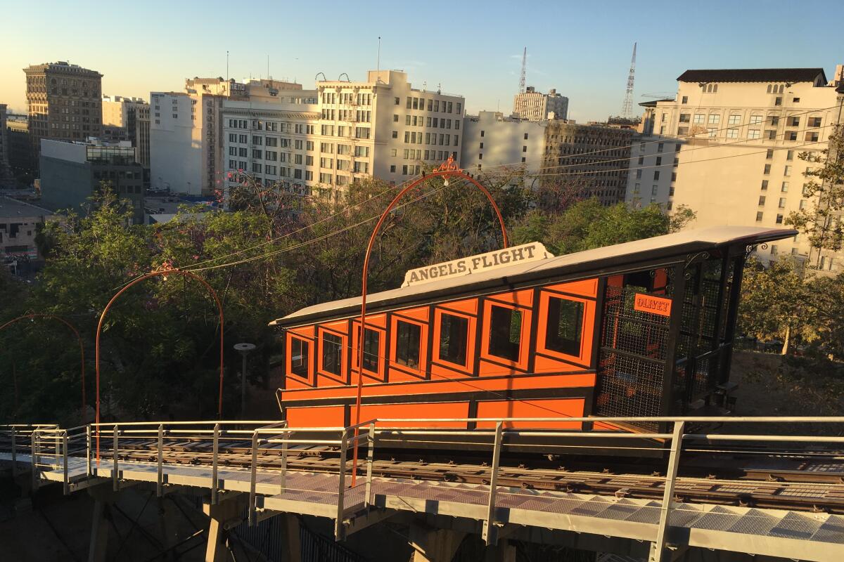 An orange cable car on a sloped track overlooking buildings in downtown Los Angeles