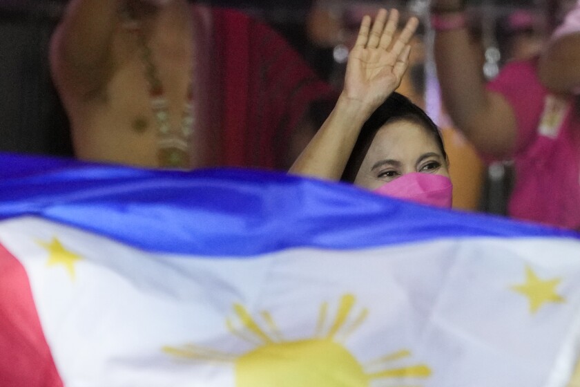 Presidential candidate, current Vice President Leni Robredo greets supporters as a Philippine flag is waved during a campaign rally that coincides with her birthday in Pasay City, Philippines on Sunday, April 24, 2022. Followers from diverse backgrounds, families with their grandparents and children, activists, doctors, Catholic church people, TV and movie stars, farmers, students, have jammed Robredo's fiesta-like campaign rallies in the tens of thousands in recent weeks. She called the emerging movement a "pink revolution" in October because many of her volunteers were clad in that color of advocacy. (AP Photo/Aaron Favila)