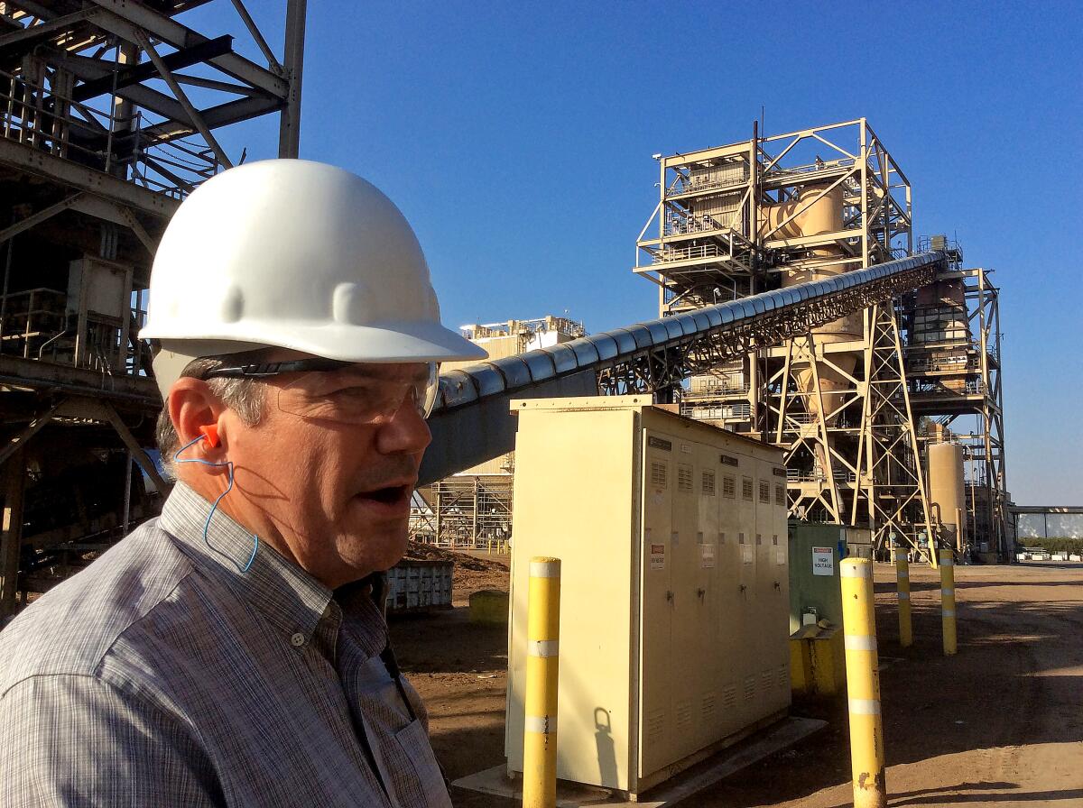 A man in a white hard hat and goggles stands at an industrial site.