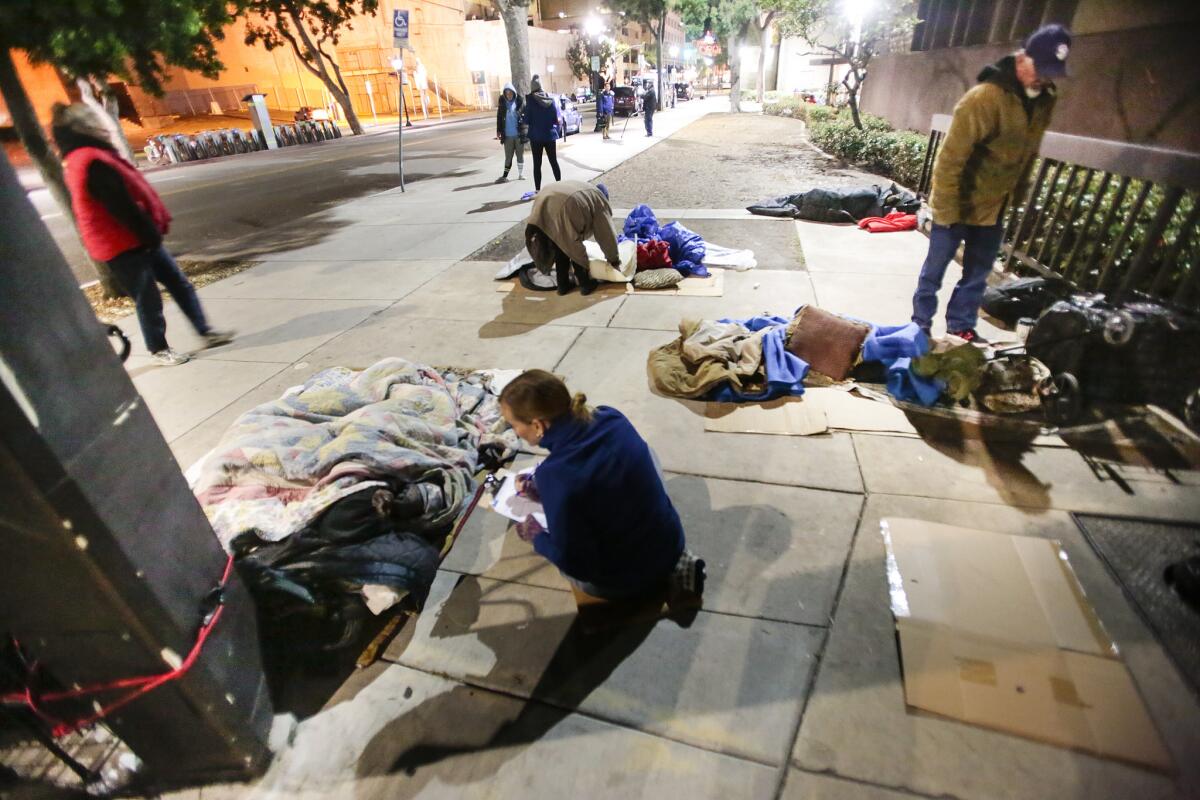 Volunteers talk with people bedded down on a sidewalk in downtown San Diego in January during the annual homeless count.