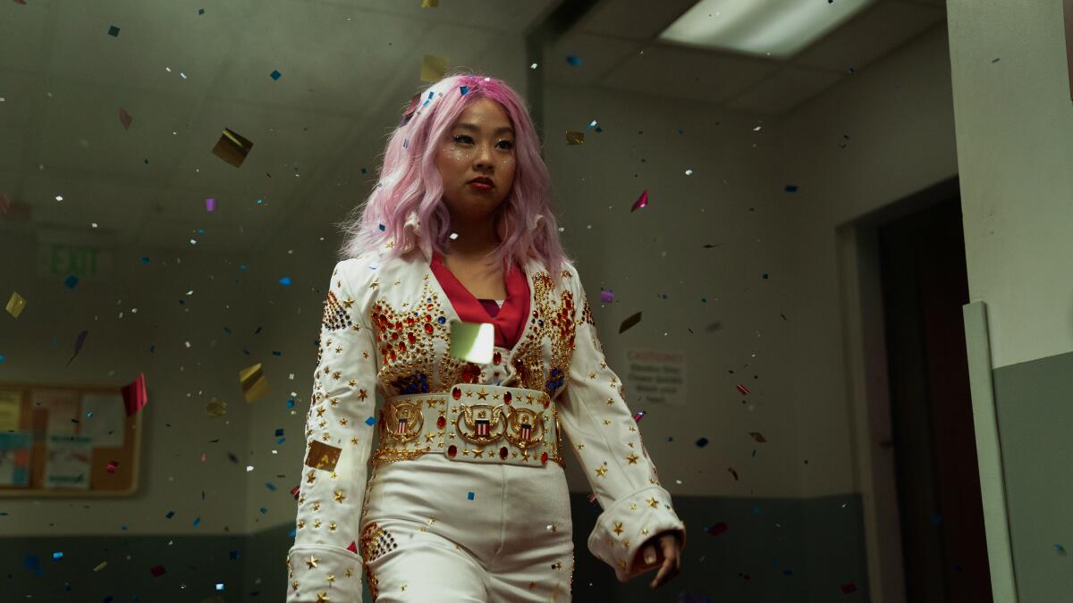 A woman with pink hair in a sequined white outfit walks amid a shower of confetti.
