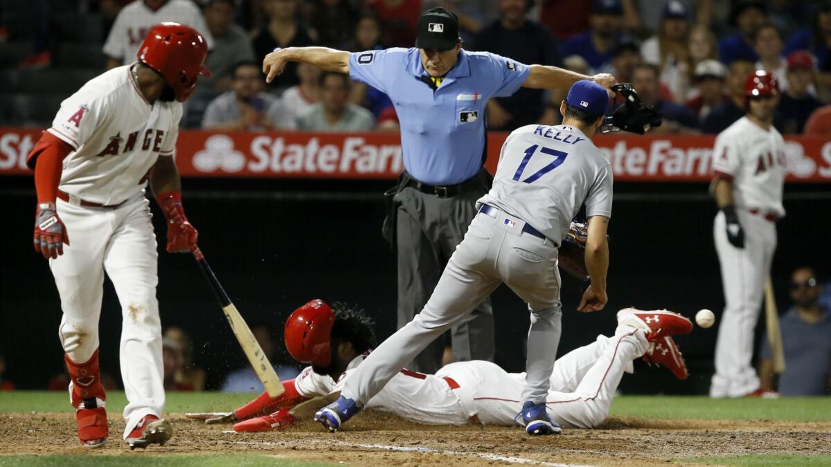 Home plate umpire Phil Cuzzi makes the call as Angels' Brian Goodwin, center, scores on a wild pitch, as the throw back to Dodgers reliever Joe Kelly gets away and Angels' Luis Rengifo, left, gets out of the way.