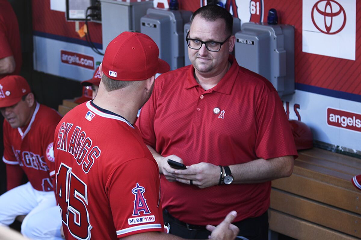 Mike Trout, wearing a jersey to honor Tyler Skaggs, speaks to Eric Kay in the dugout before a game.